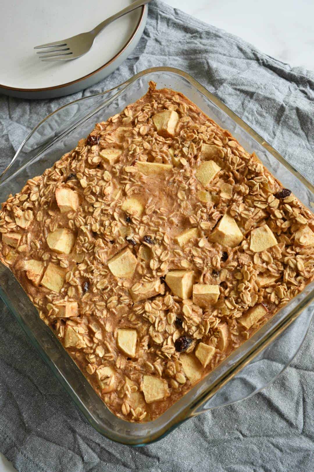 Apple pie baked oatmeal in a baking dish with a plate on the side.