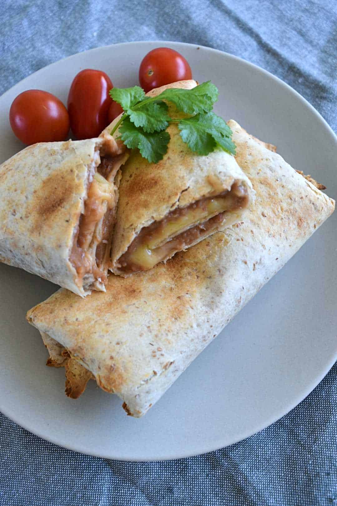 Bean and cheese chimichangas on a plate with tomatoes and cilantro.