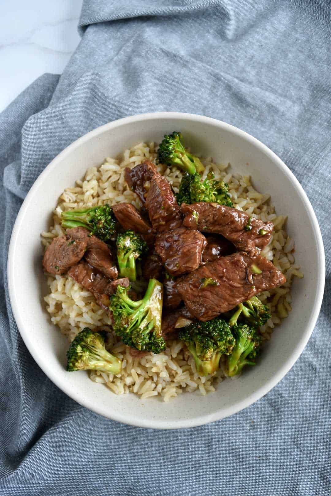 Broccoli and beef stir fry in a white bowl with rice.