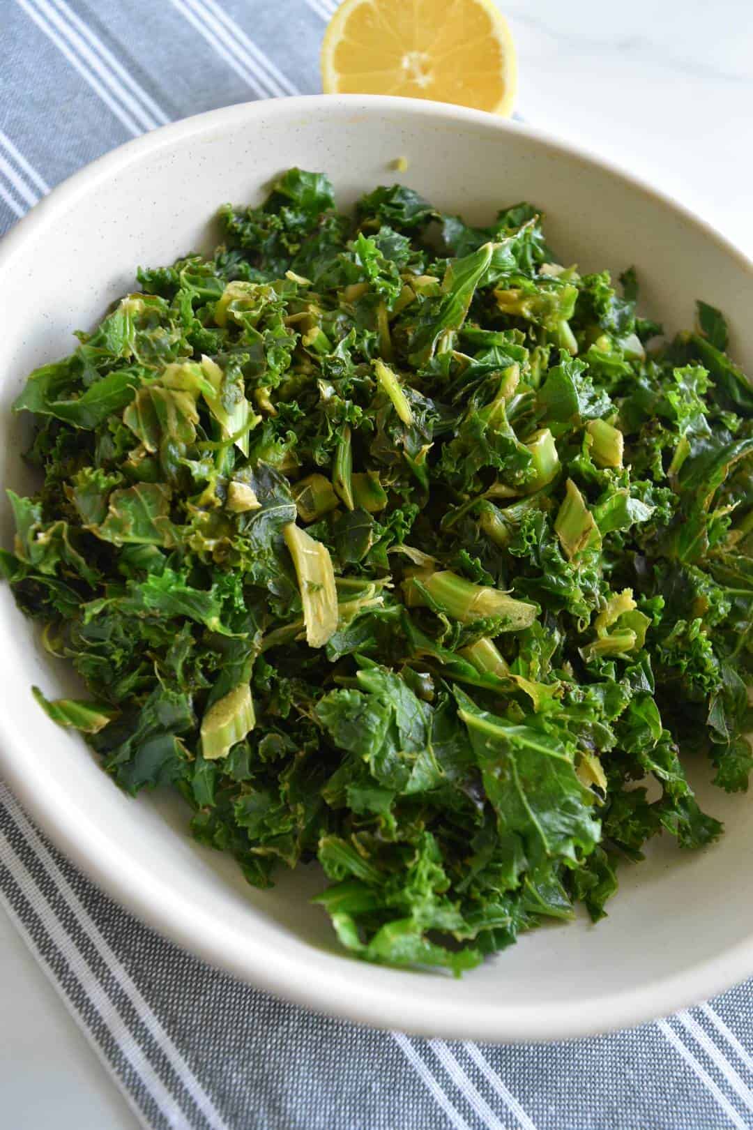 Braised kale in a bowl with lemon on the side.