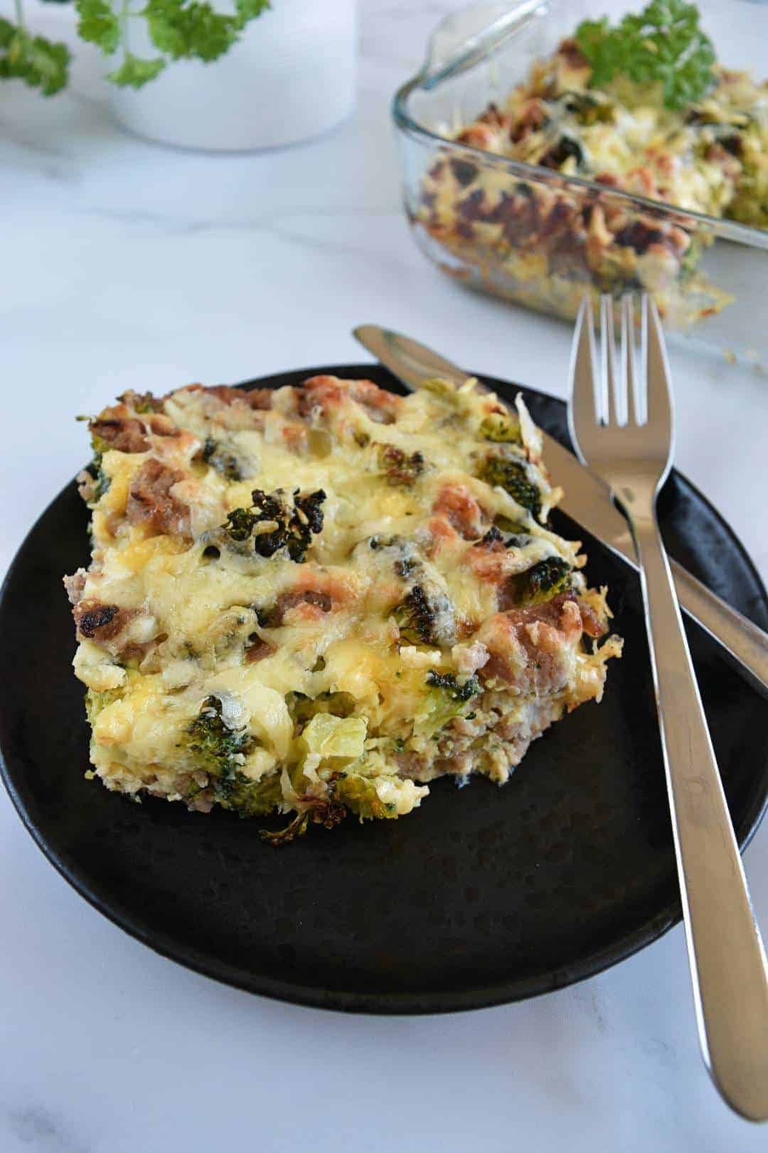 Breakfast casserole with sausage and broccoli on a black plate with cutlery.