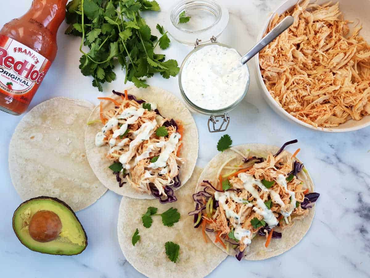 Buffalo chicken tacos on a marble table with ranch, buffalo chicken and buffalo sauce on the side.