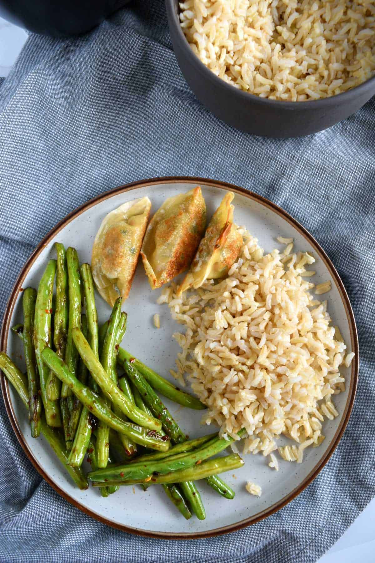 Green beans, potstickers and rice on a plate with a bowl of rice in the background.