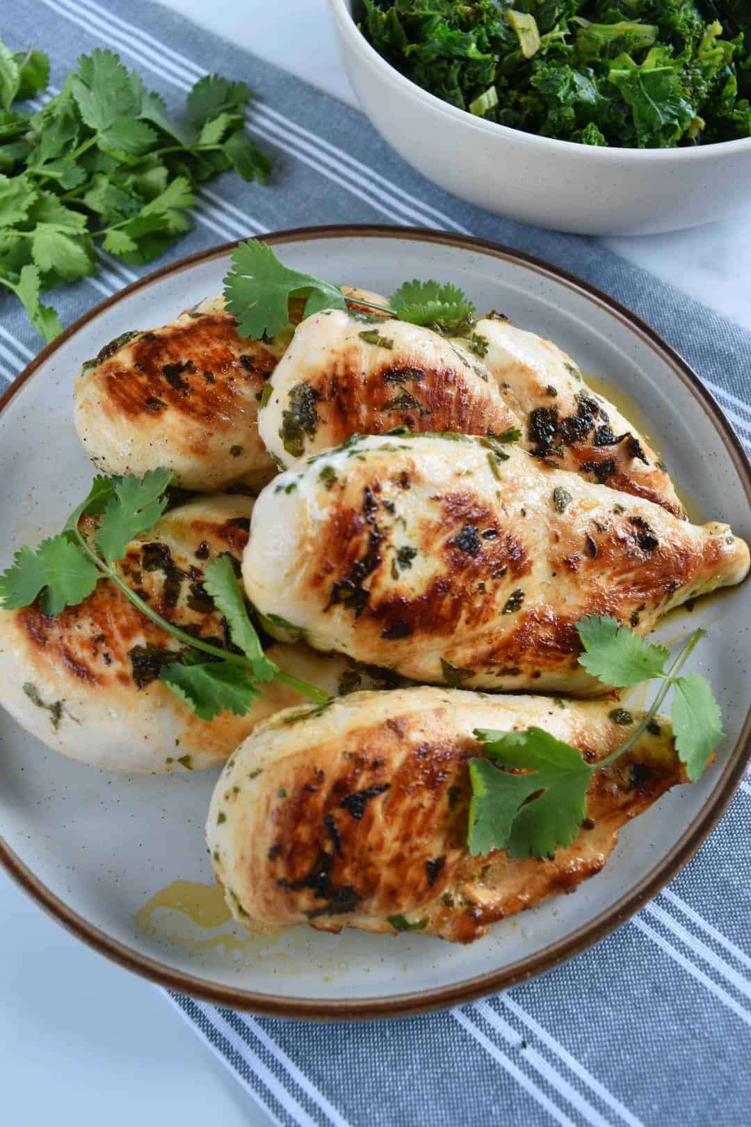 Cilantro lime chicken breasts on a plate with fresh herbs and salad on the side.