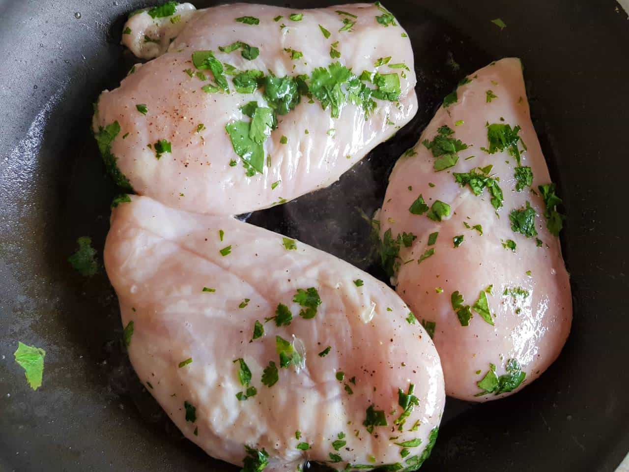 Chicken breast fillets with cilantro in a frying pan.