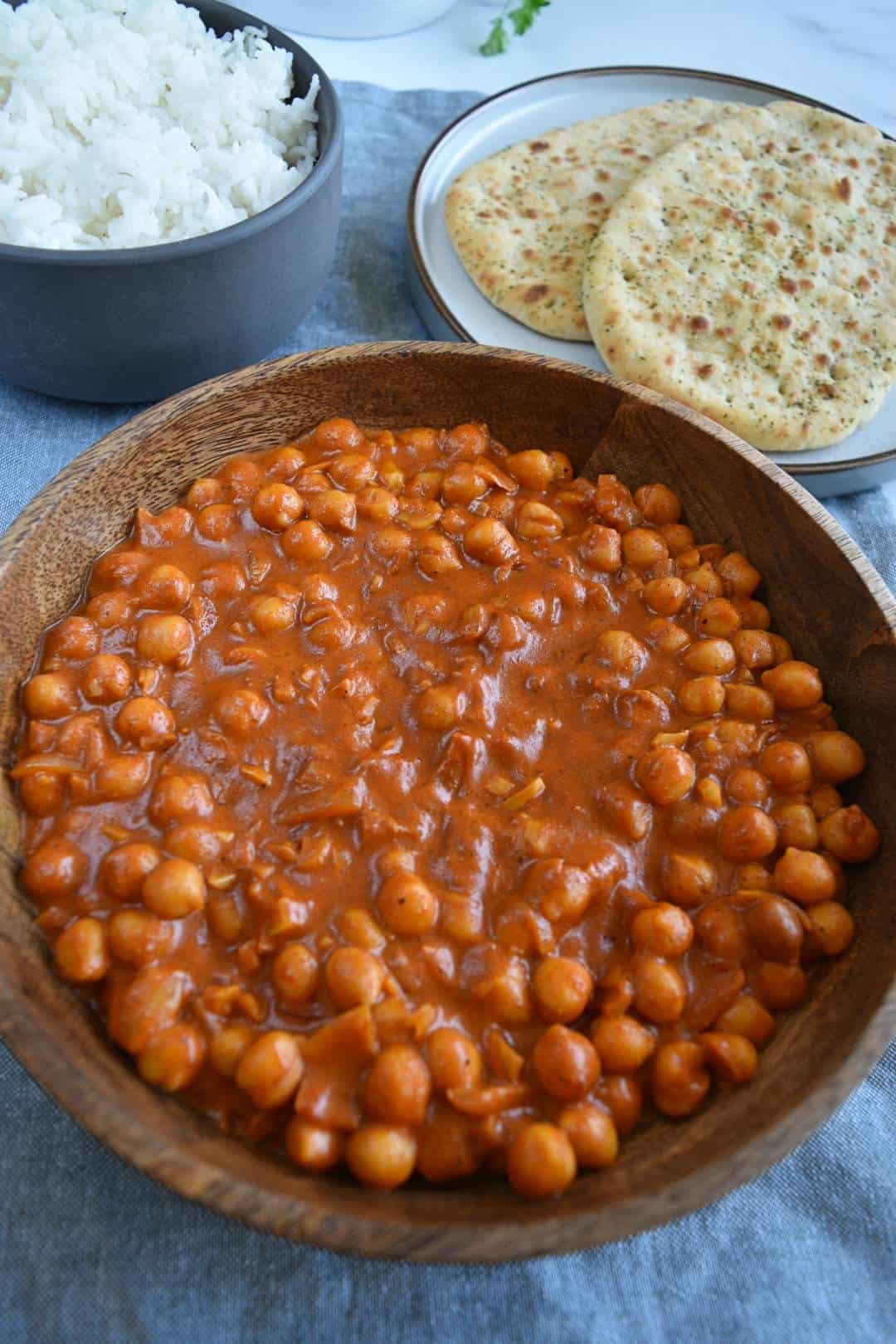 Chana masala in a wooden bowl with rice in the background.