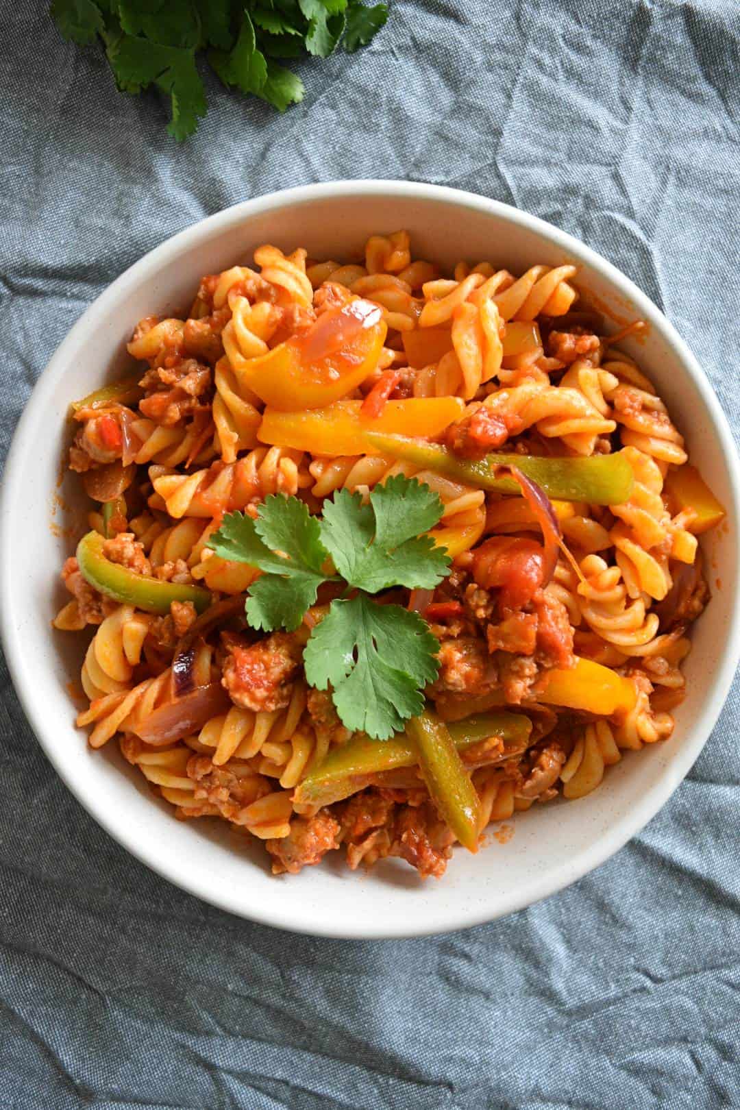 Pasta with sausages and peppers in a bowl on a tablecloth.