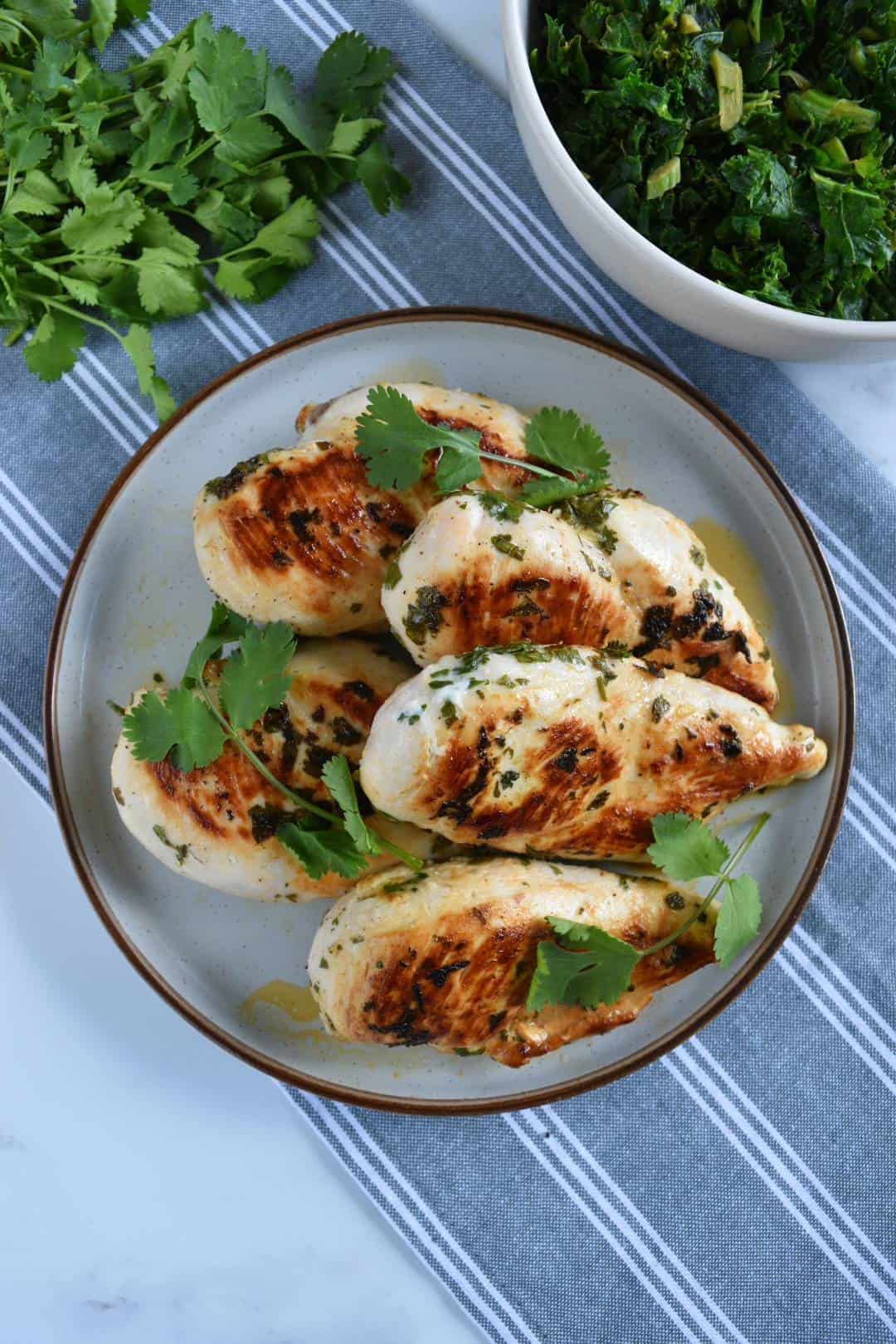 Cilantro lime chicken on a plate with a bowl of salad and fresh herbs on the side.