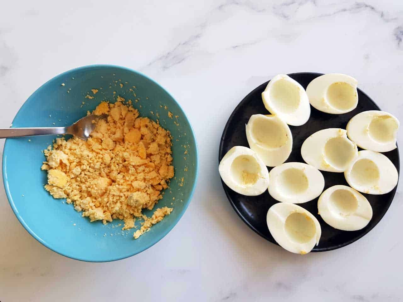 Boiled eggs with the yolks removed, and a bowl containing the yolks on the side.