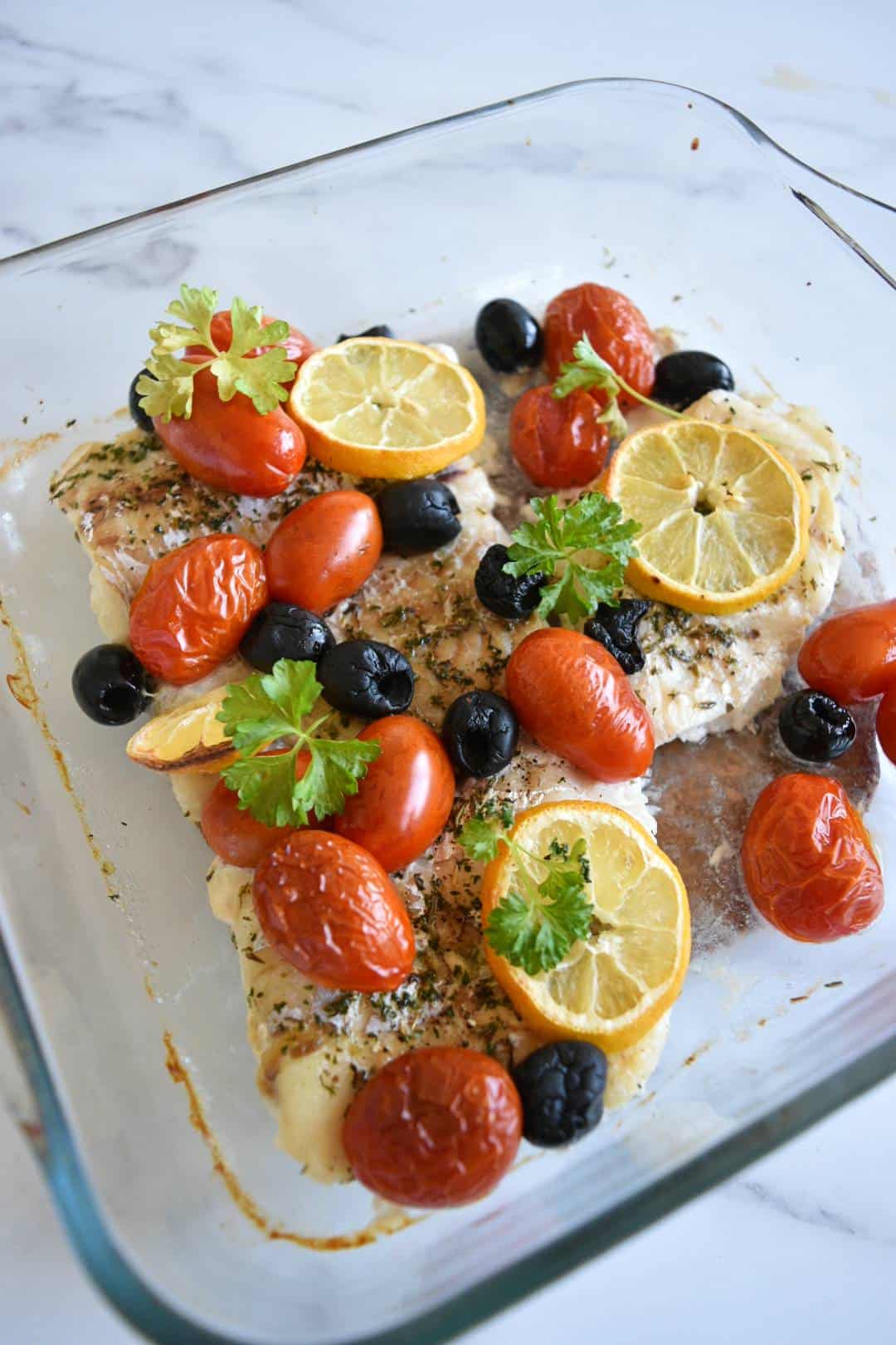 Mediterranean baked cod with olives and tomatoes in an oven proof dish.