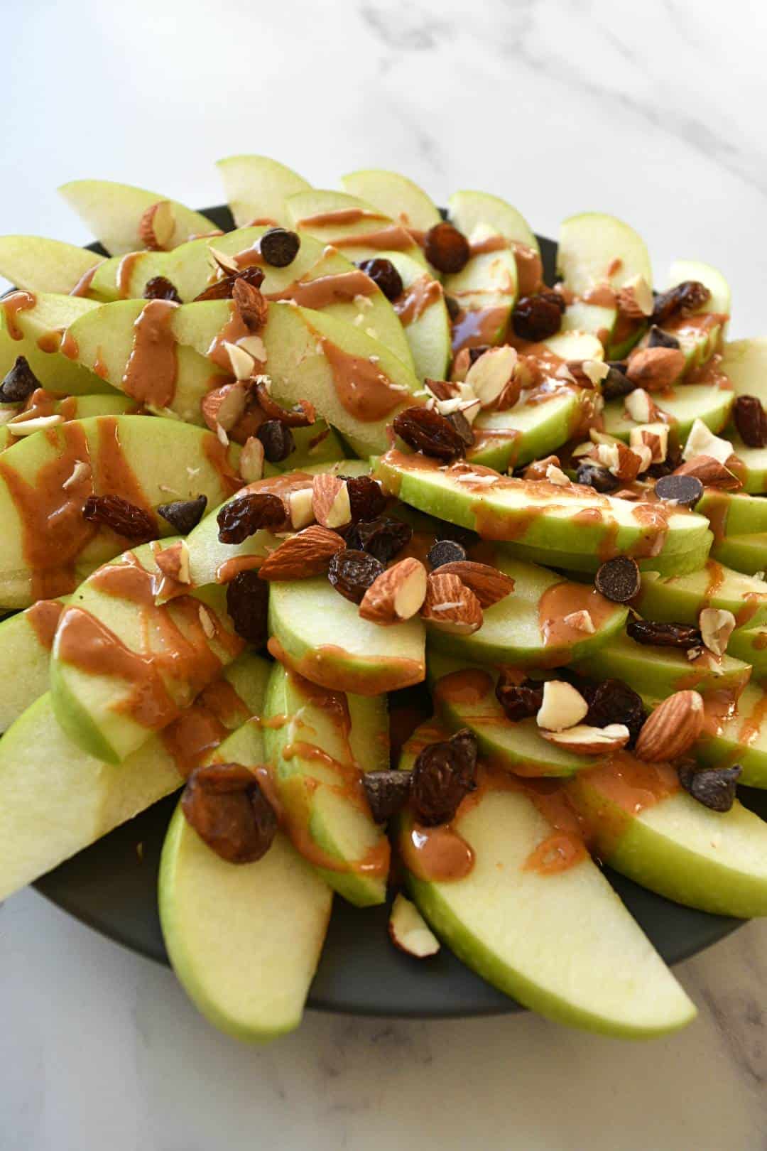 Peanut butter apple nachos topped with raisins, almonds and chocolate chips.