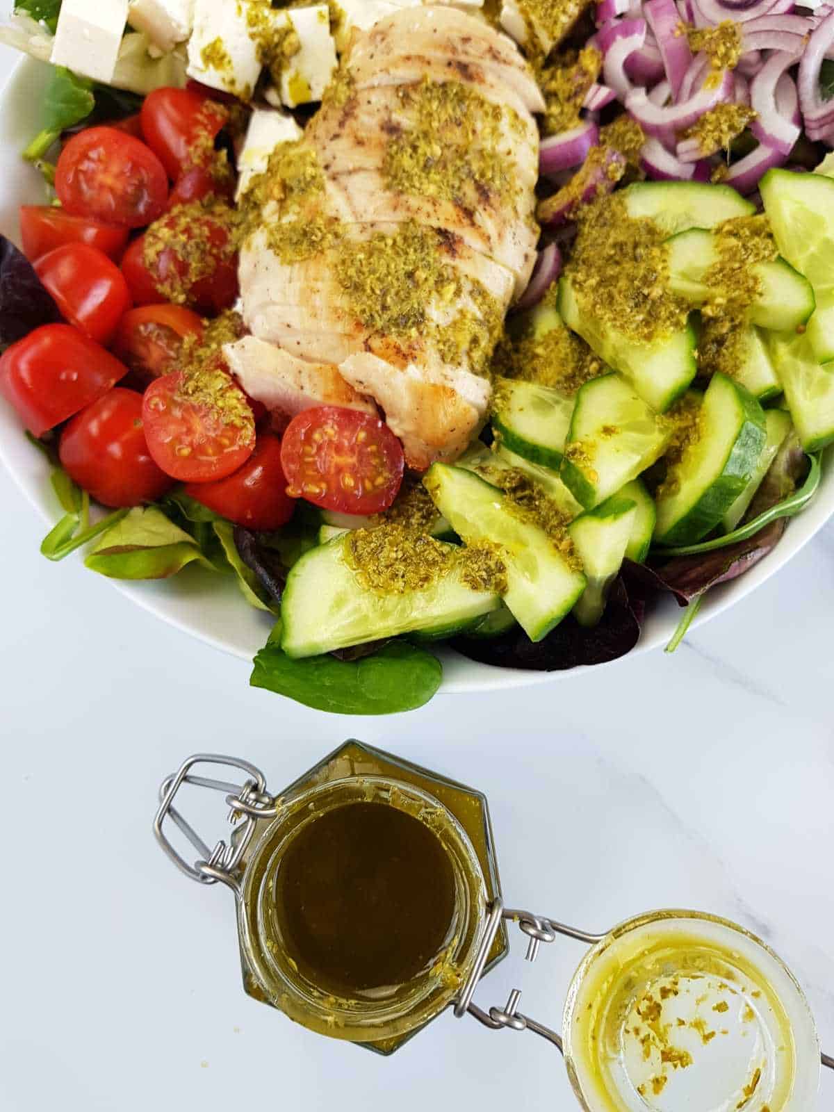 Pesto salad dressing in a jar next to a salad with a vinaigrette drizzle on top.