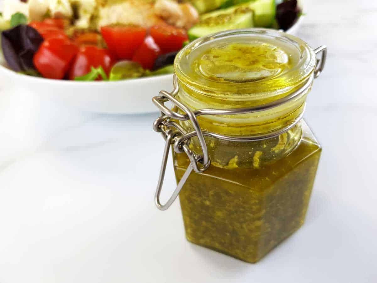 Pesto salad dressing in a jar with a bowl of salad in the background.