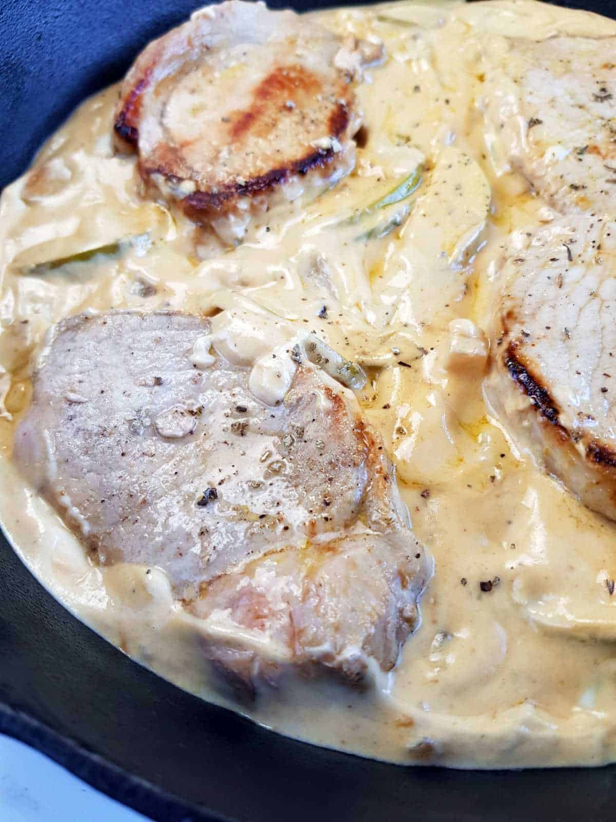 Cooked boneless pork chops in creamy apple sauce in a cast iron skillet.