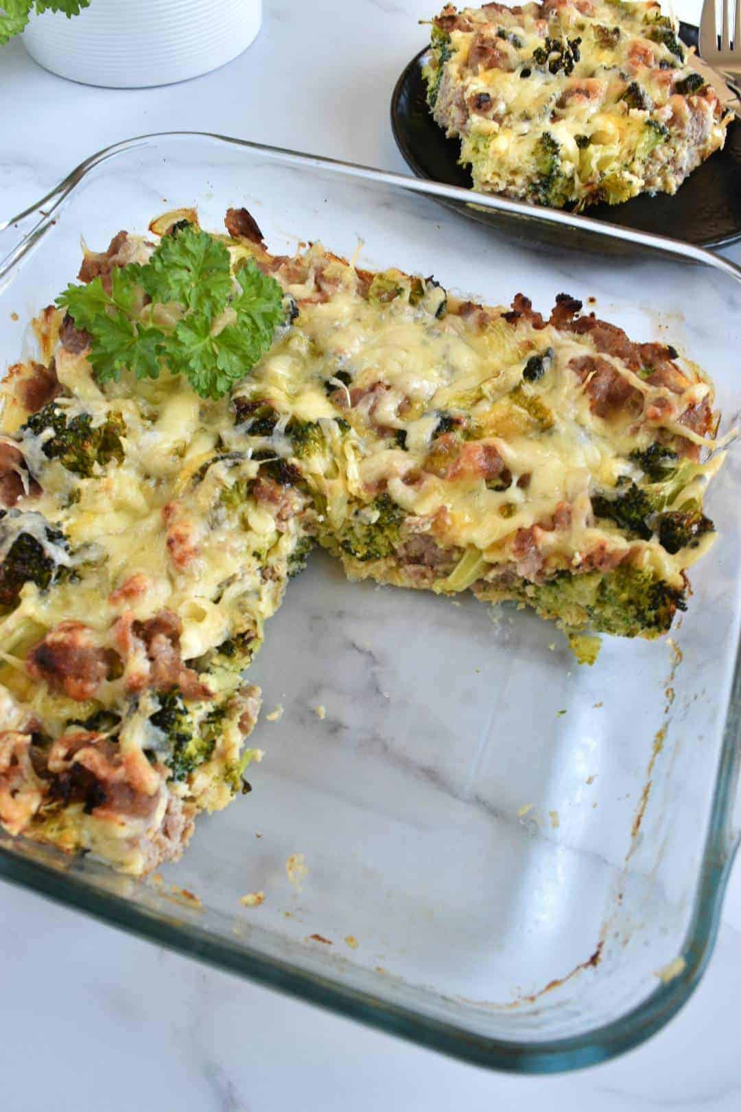 Broccoli and sausage casserole in a dish, with one serving plated on the side.