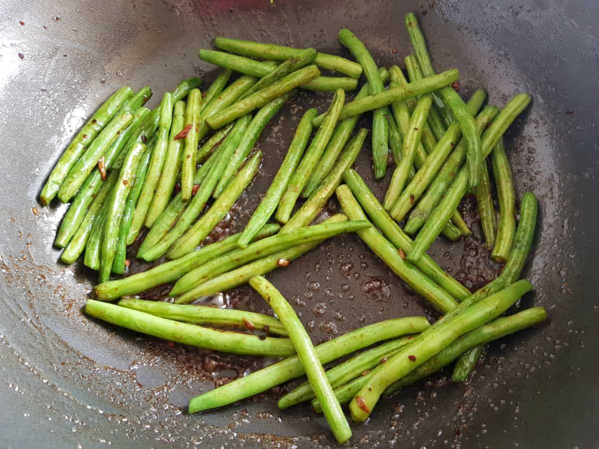 Green beans in a wok covered with stir fry sauce.