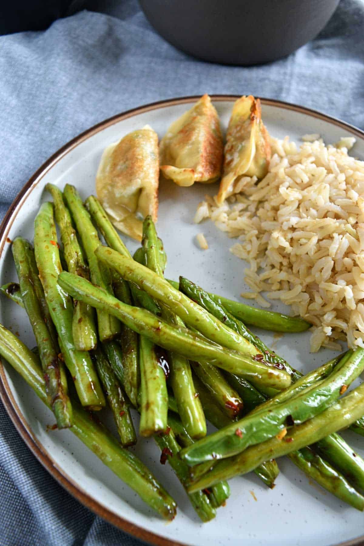 Green beans, potstickers and rice on a plate.