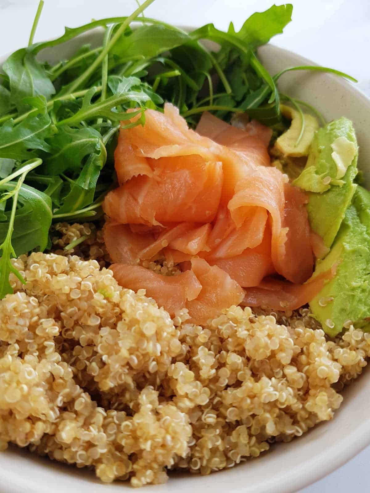 Smoked salmon and quinoa salad with avocado and arugula in a bowl.