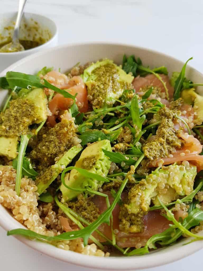 Smoked salmon and quinoa salad topped with pesto dressing. A bowl of dressing in the background.