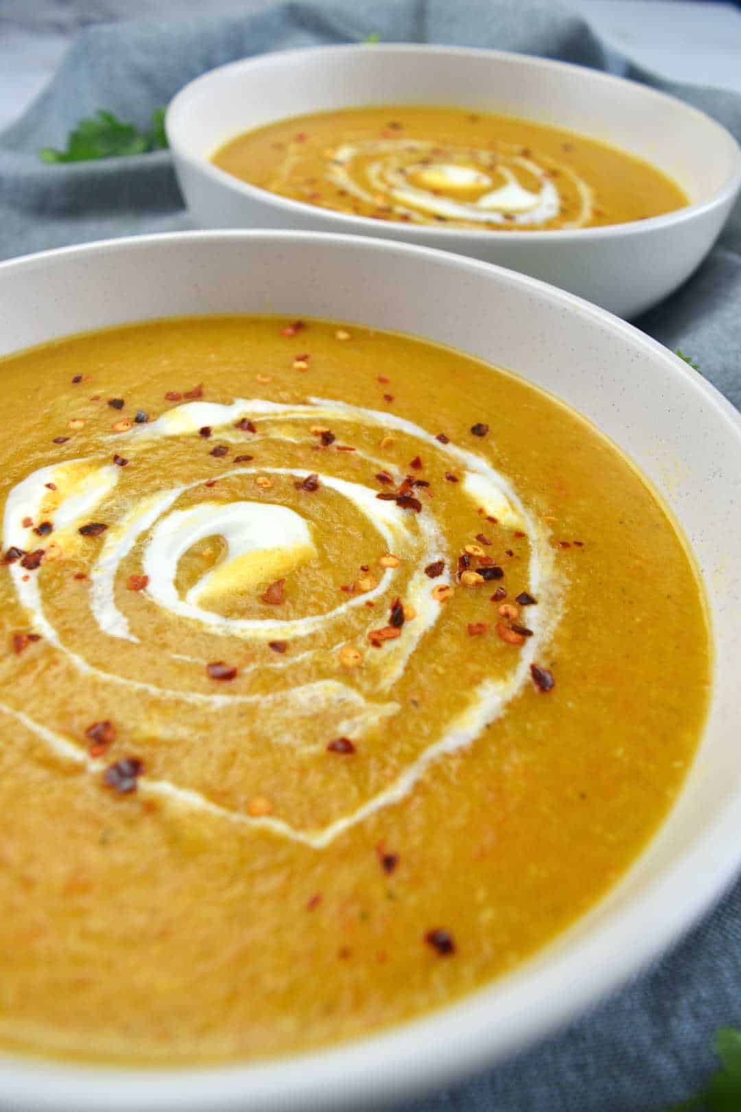 Red lentil soup in white bowls with chili flakes on top.