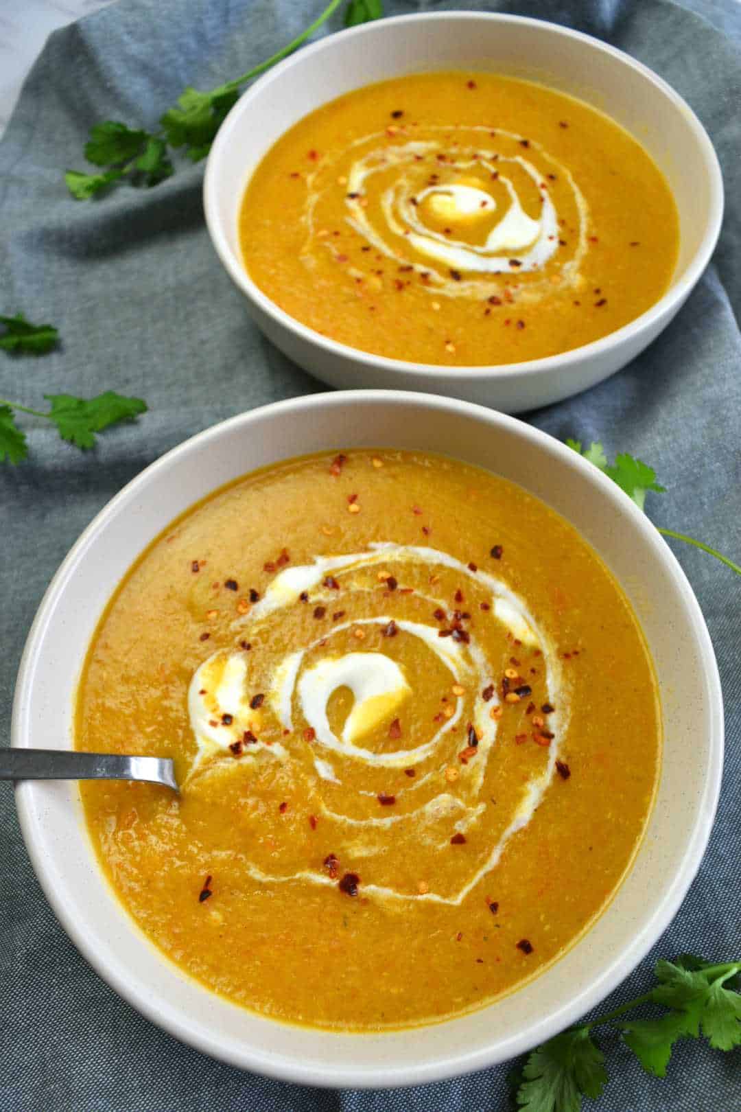 Spicy red lentil soup in bowls, garnished with chili flakes and yogurt.