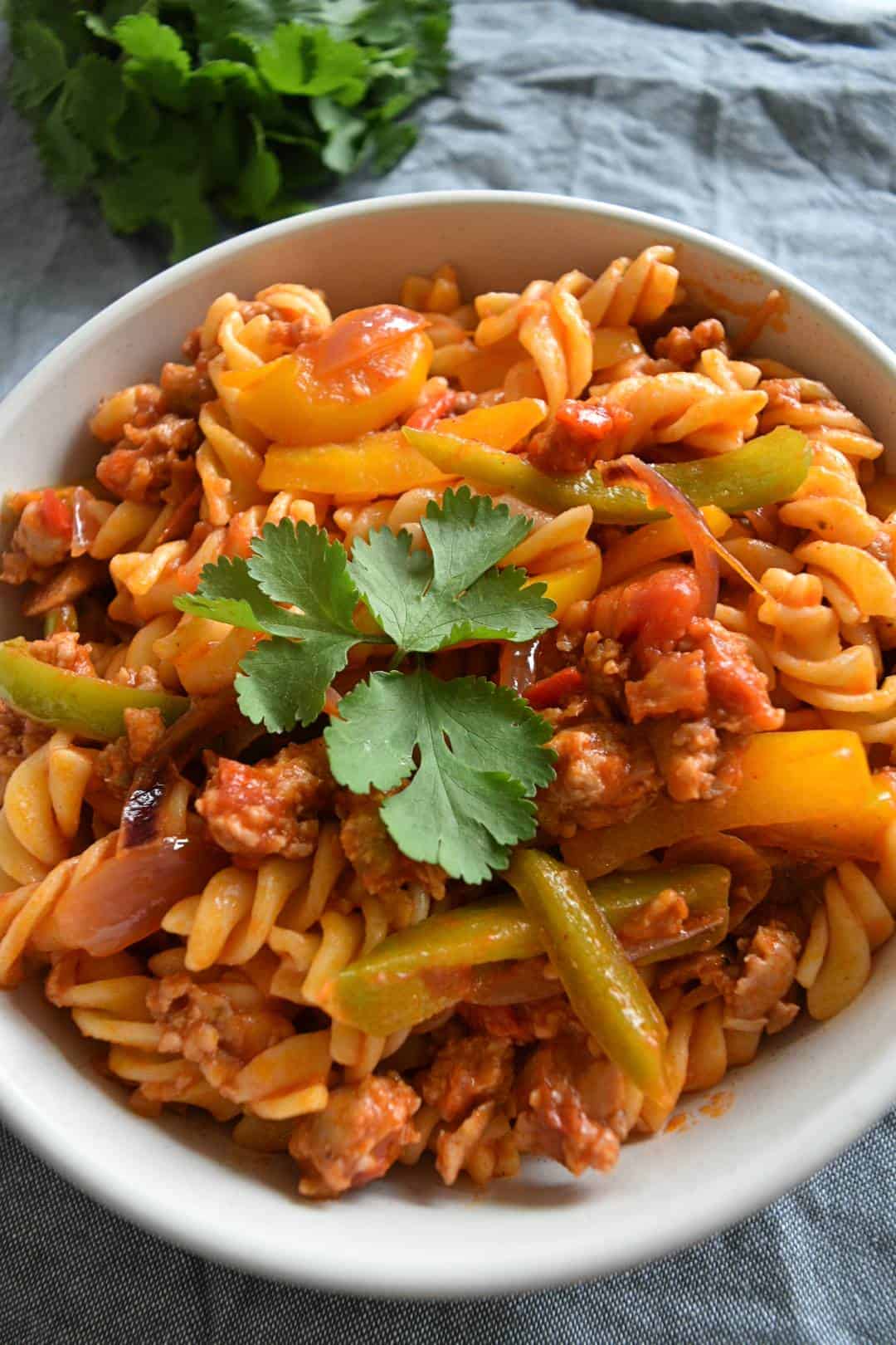 Spicy sausage pasta in a white bowl with cilantro garnish.