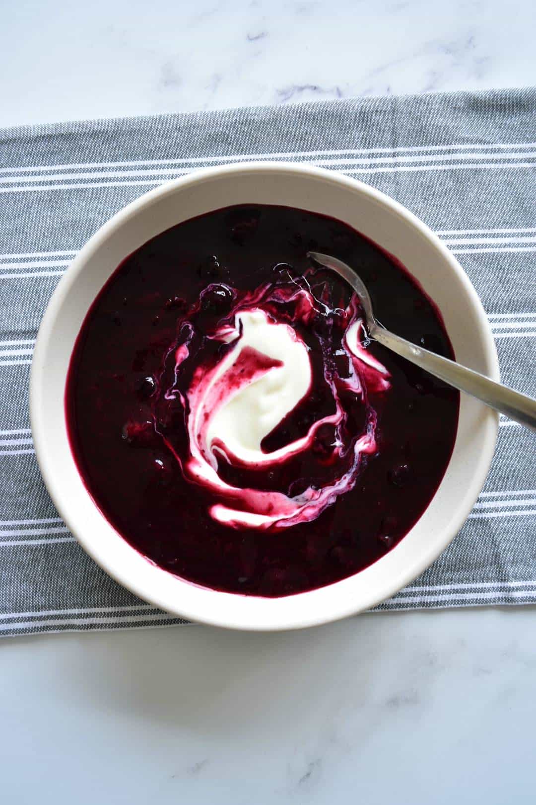 Chilled Swedish blueberry soup in a bowl with swirled yogurt on top.