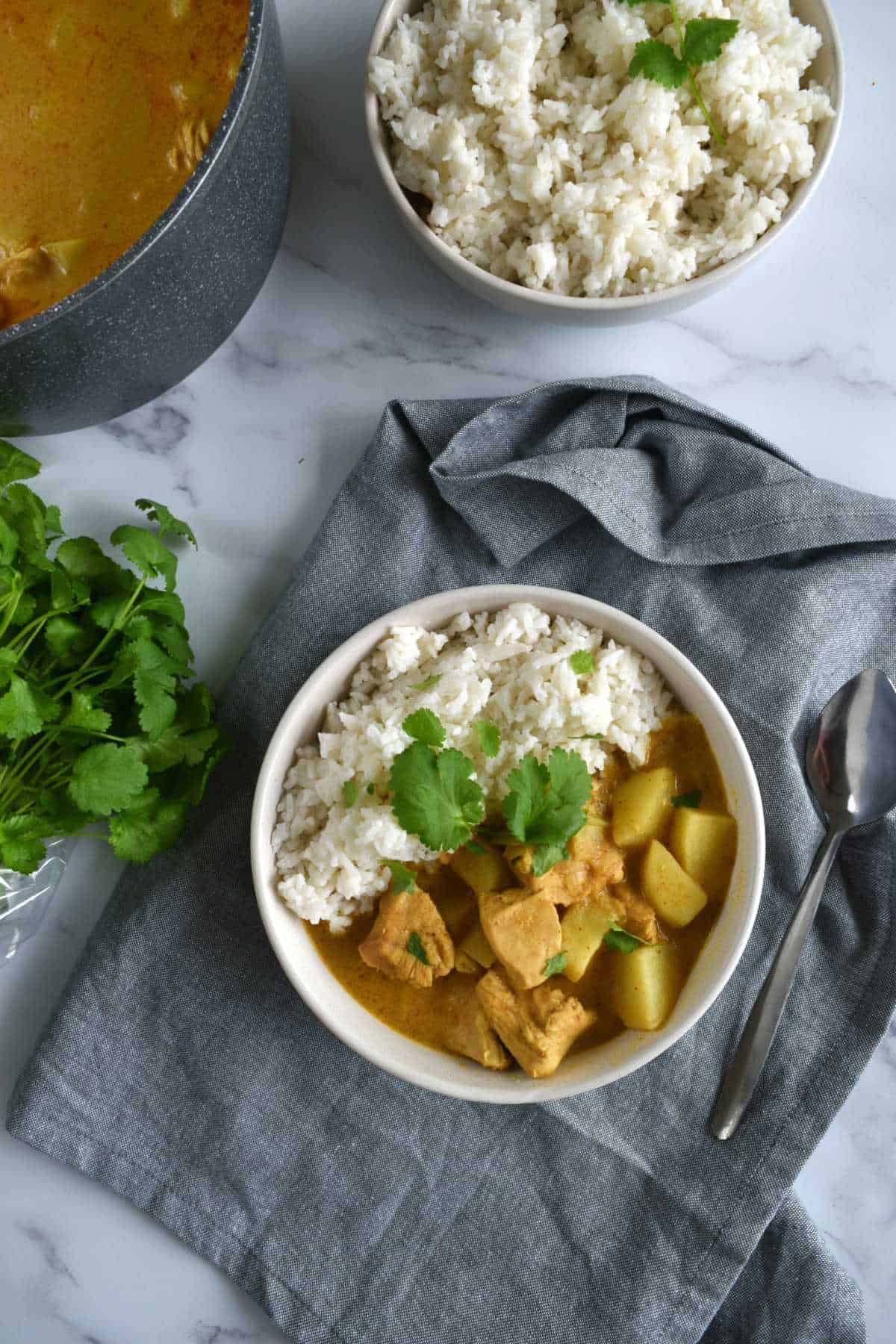 A bowl of chicken curry and rice, with a large pot of Thai curry and more rice in the background.