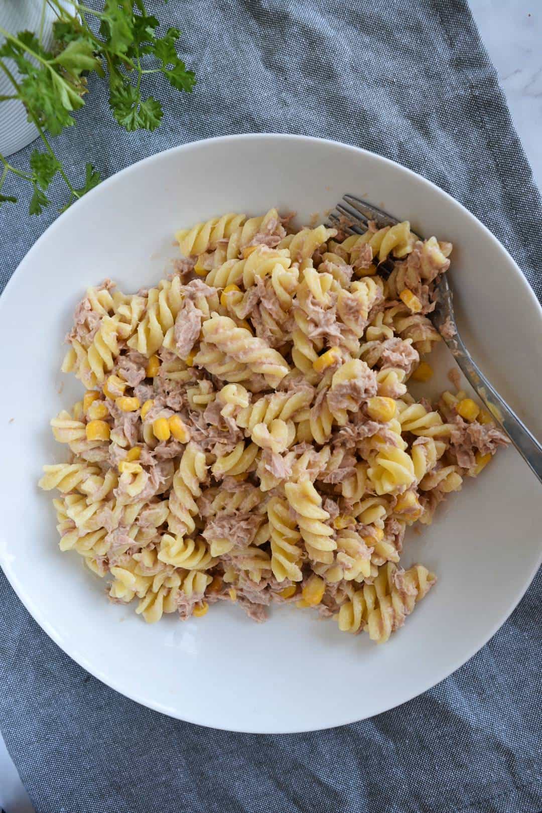 Tuna pasta salad in a bowl with fresh herbs on the side