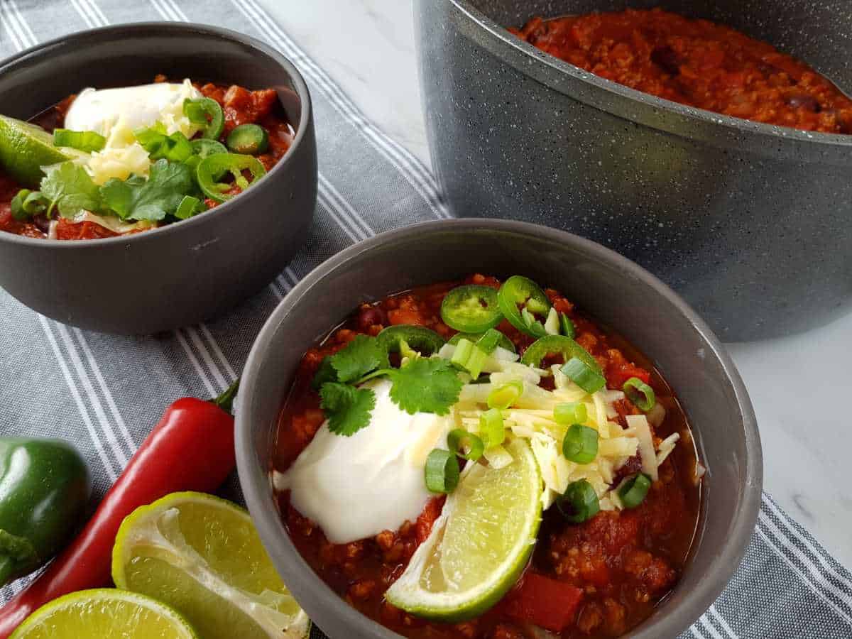 Two bowls of chili with a large pot on the side.