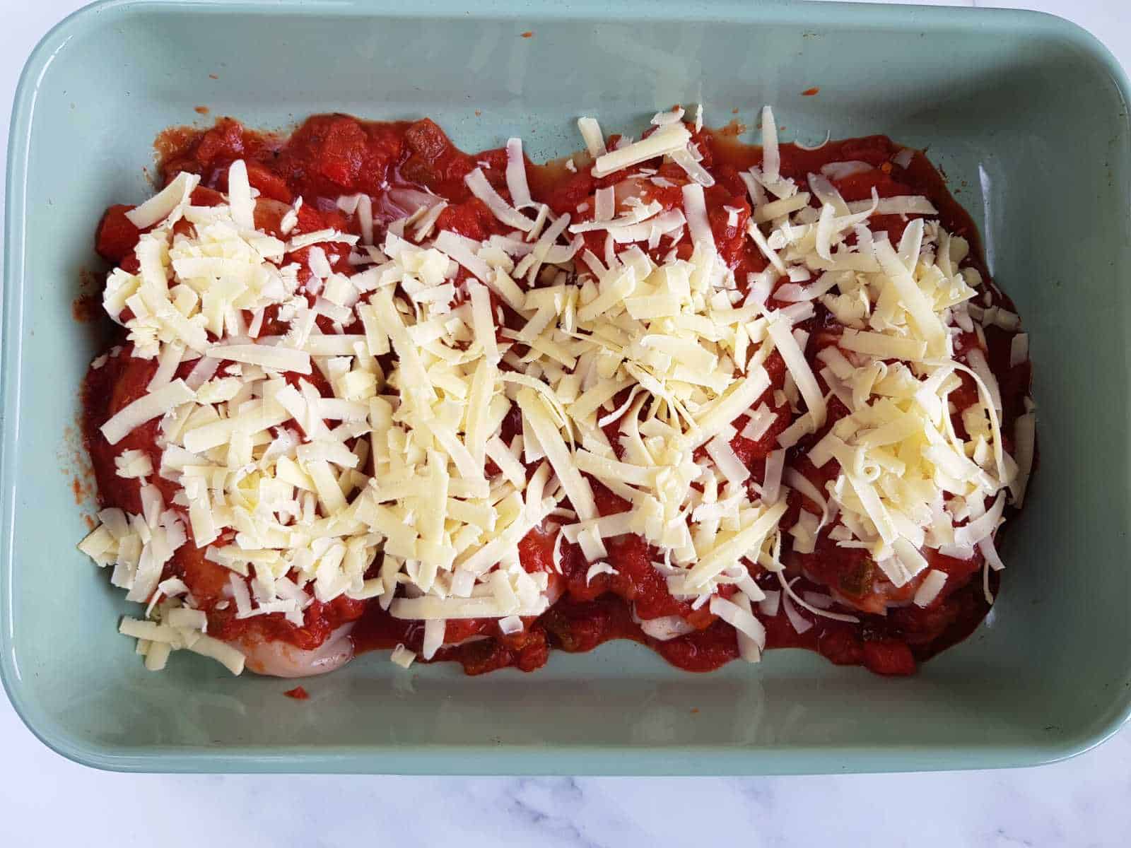 Uncooked chicken covered with salsa and cheese in a casserole dish.