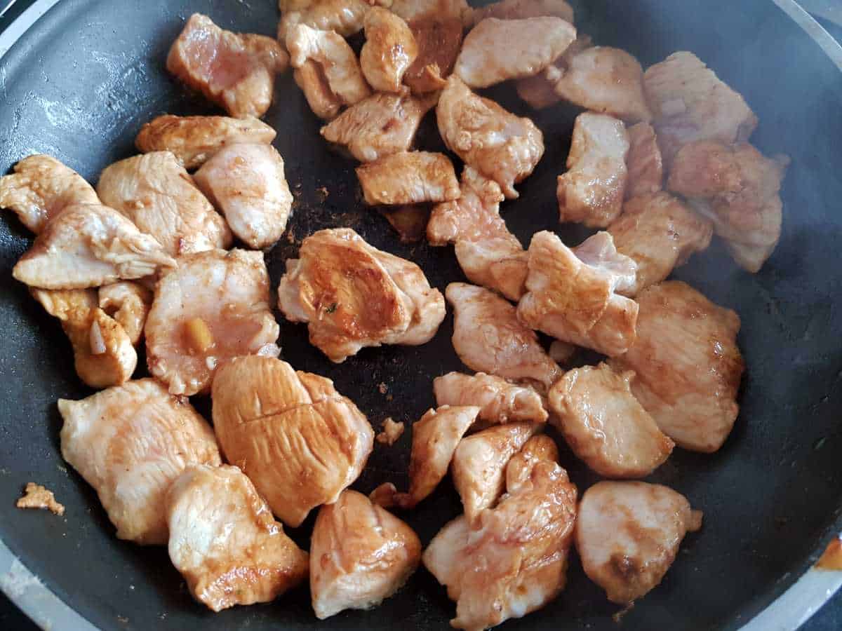 Chicken pieces cooking in a frying pan.