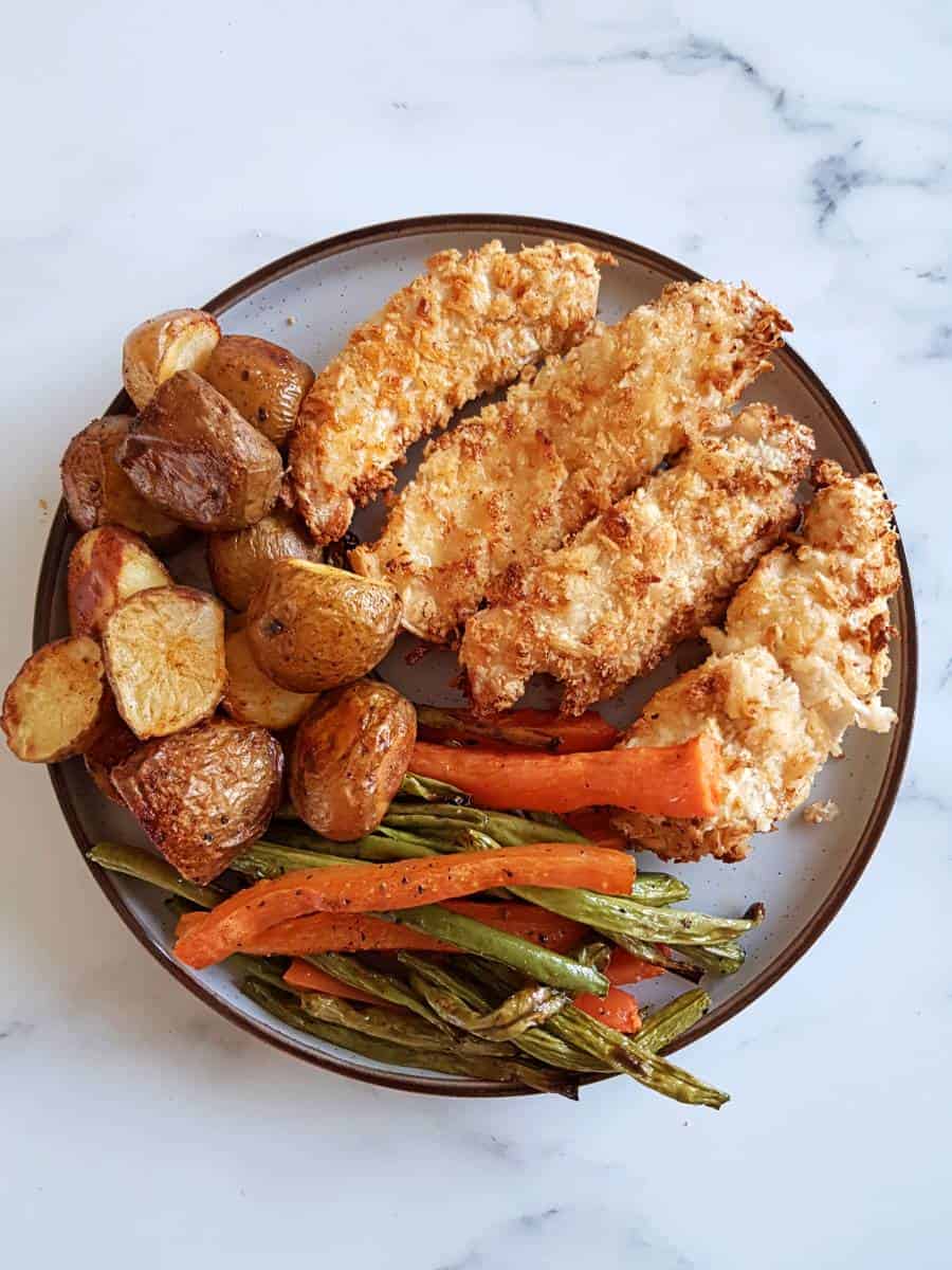 Air fryer breaded chicken on a plate with roasted carrots, green beans and potatoes.