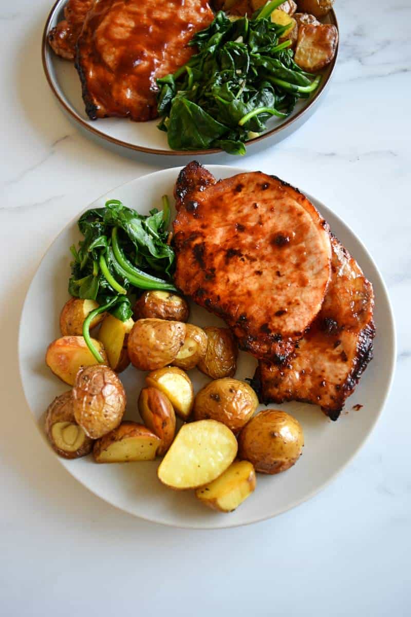 Air fryer pork chops on a plate with spinach and potatoes.