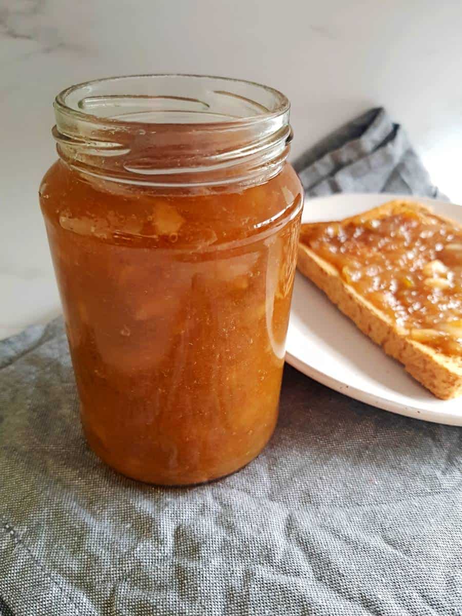 A jar of apple and rhubarb jam with a slice of toast in the background.