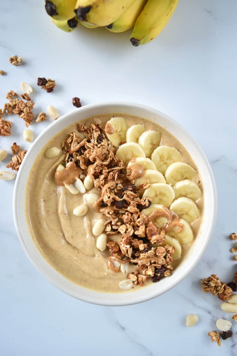 Banana peanut butter smoothie bowls with bananas and peanuts on the side.