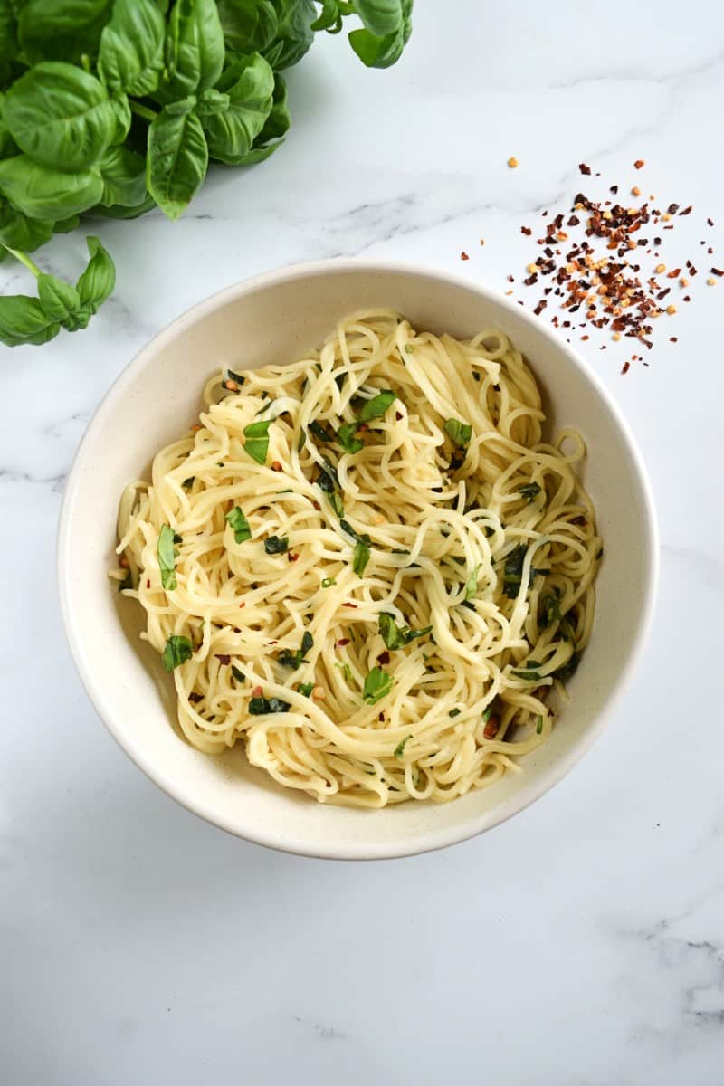 Basil and garlic pasta in a white bowl on a marble table.