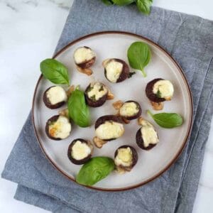 Basil and mozzarella stuffed mushrooms on a plate with basil leaves.