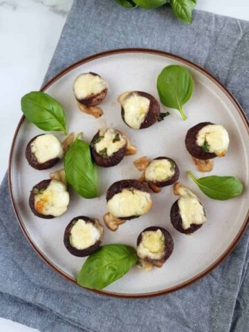 Basil and mozzarella stuffed mushrooms on a plate with basil leaves.