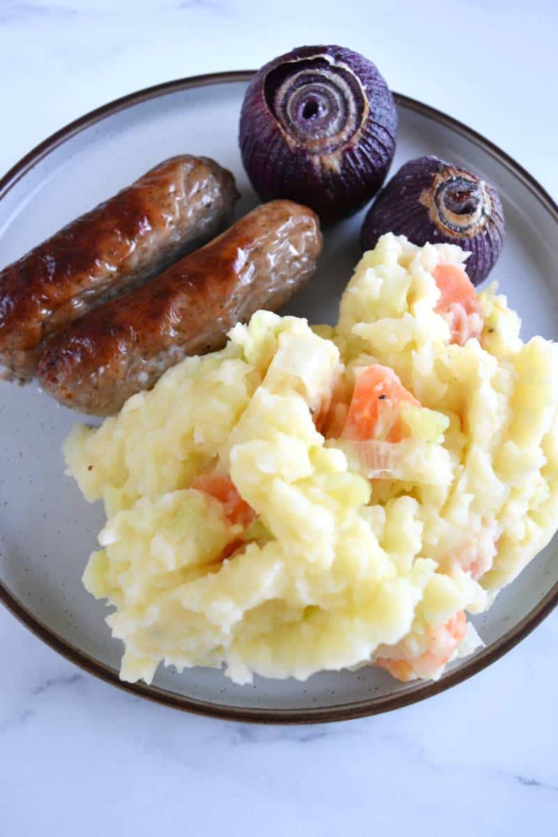 Stoemp, sausage and red onions on a plate.