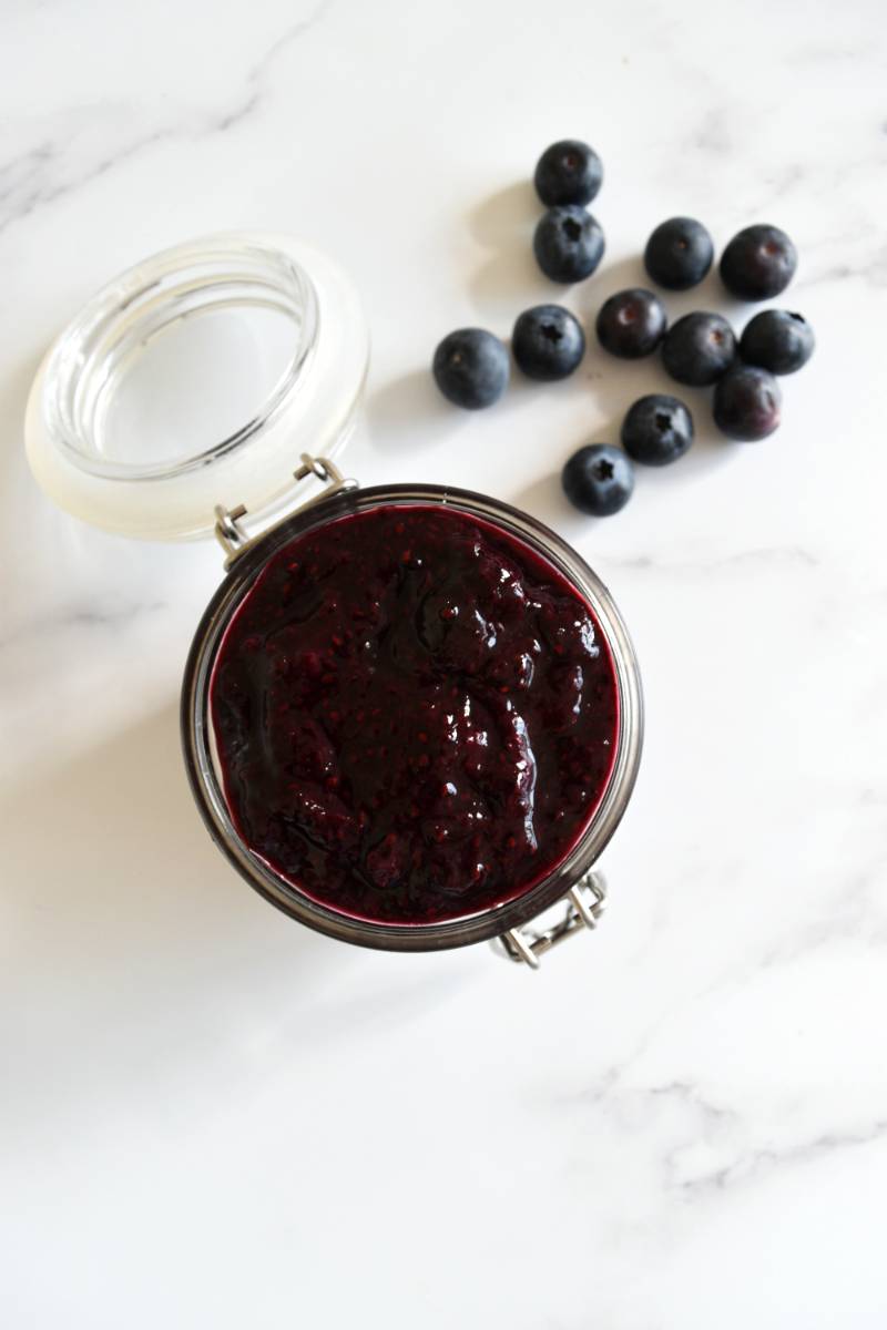 Blueberry and chia jam in a jar on a marble table.