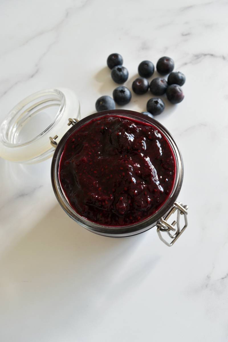 Blueberry chia jam in a jar with blueberries on the side.