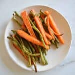 Carrots and green beans on a white plate on a marble table.