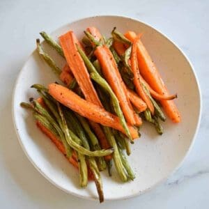 Carrots and green beans on a white plate on a marble table.