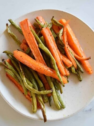 Carrots and green beans on a white plate on a marble table.