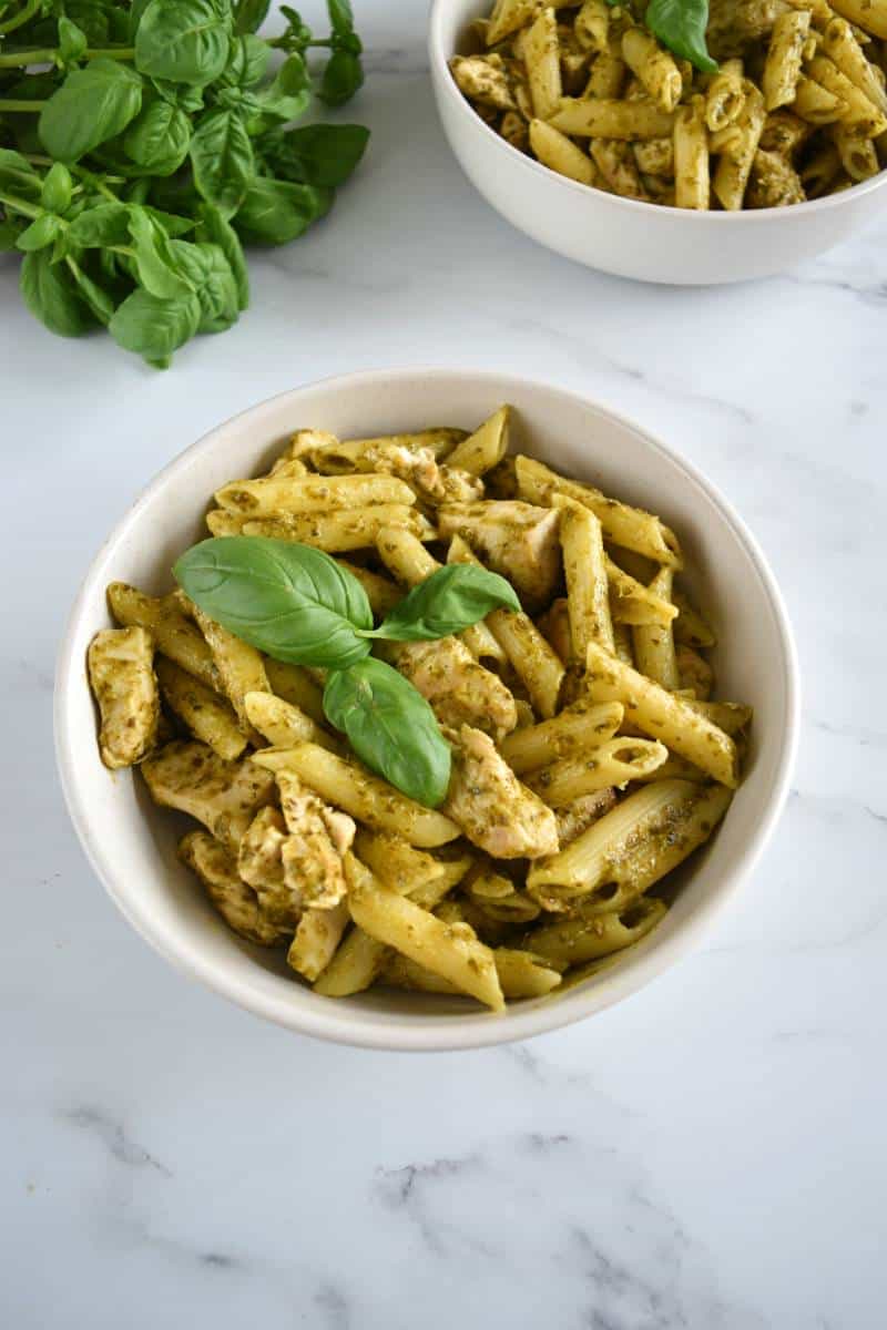 Chicken and pesto pasta in a bowl with fresh basil in the background.