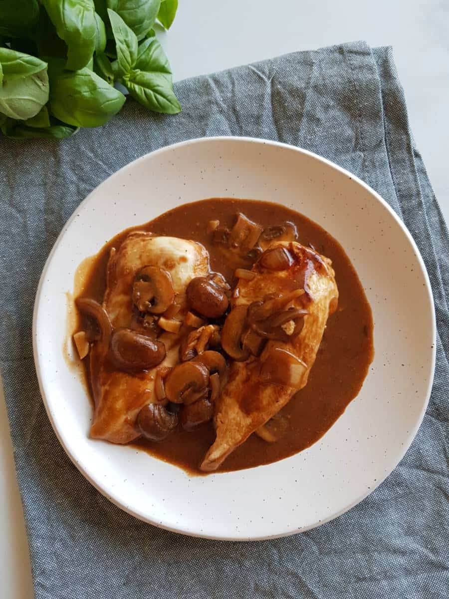 Marsala chicken on a plate with fresh basil in the background.