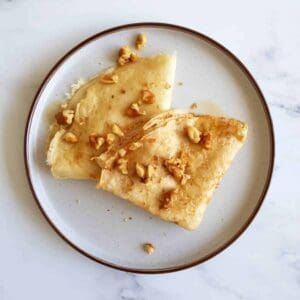 Two thin pancakes with walnuts on a plate.