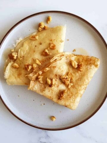 Two thin pancakes with walnuts on a plate.