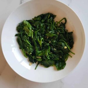 Garlic sauteed spinach in a bowl on a marble table.